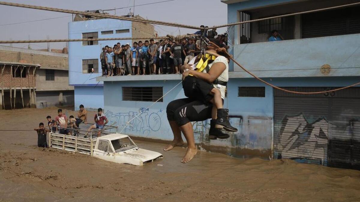 Una mujer y su hija reciben ayuda para pasar una calle inundada, el 17 de marzo de 2017 en Lima, Perú.