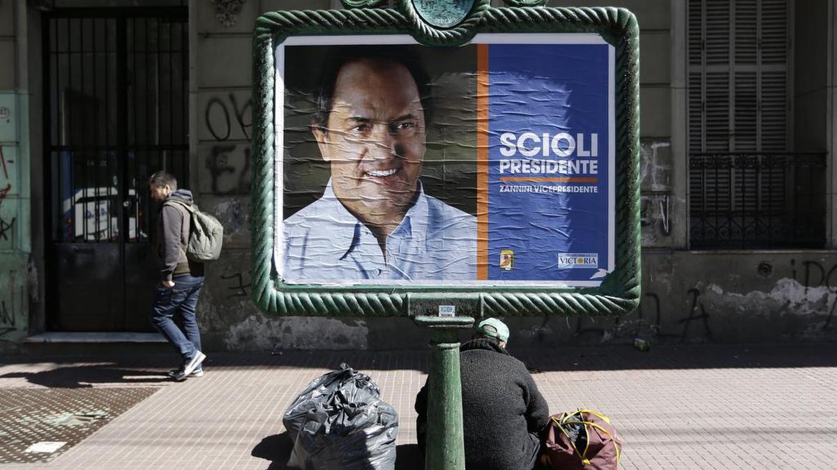 Un desamparado se sienta el viernes en Buenos Aires detrás del cartel político del candidato presidencial Daniel Scioli.