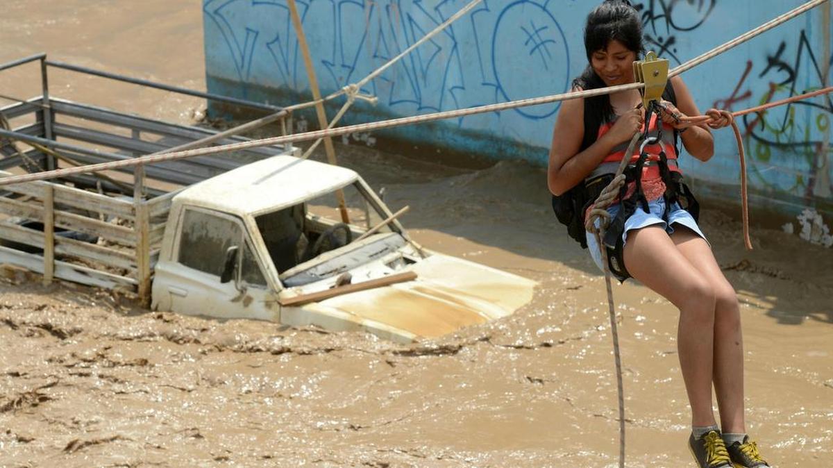 Los residentes del distrito populoso de Huachipa, al este de Lima, son ayudados el 17 de marzo de 2017 por la policía y los equipos de rescate de bomberos para cruzar las inundaciones repentinas que golpean su vecindario y aislar a sus residentes. El fenómeno climático El Niño está causando desbordamientos de ríos fangosos en toda la costa peruana, aislando a cientos de personas, en su mayoría residentes en los barrios industriales de Limas.