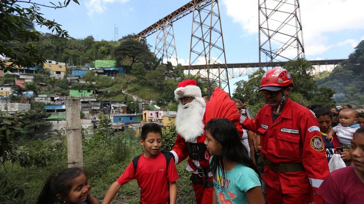 El bombero Héctor Chacón (c), de 70 años, vestido como Papa Noel y después de haber descendido de un puente de 150 metros hacia un asentamiento entrega regalos a niños que viven en precarias condiciones hoy, miércoles 23 de diciembre de 2015, en la Ciudad de Guatemala.