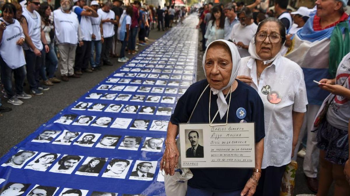 Miembros de las Madres de Plaza de Mayo y de Abuelas de la Plaza de Mayo, organizaciones de derechos humanos y miles de manifestantes se encuentran junto a una gran pancarta con retratos de personas desaparecidas durante la dictadura militar de 1976-1983.