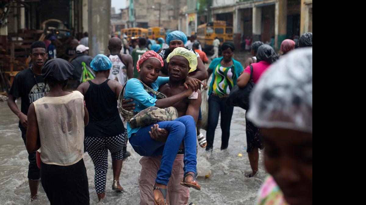 
Una joven es cargada por un hombre para cruzar una calle inundada en Puerto Príncipe, tras pagarle 10 centavos, el sábado. 
