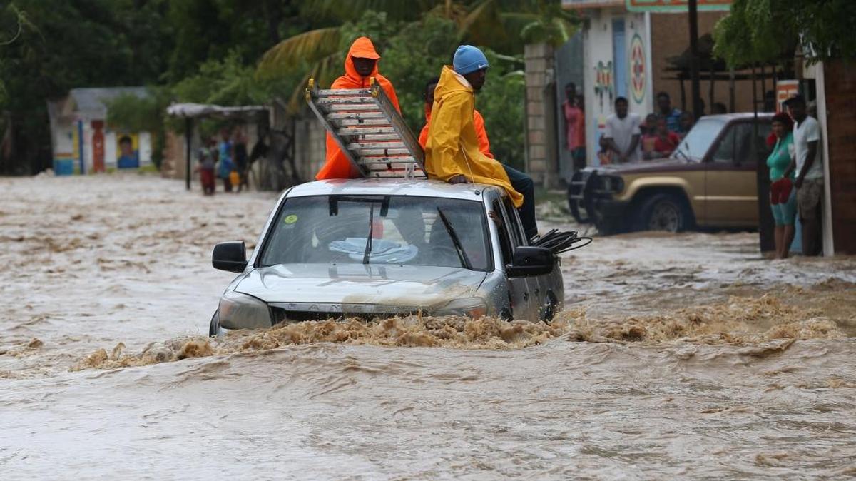 Personas intentan cruzar una calle inundada en Leogane tras el paso del huracán Matthew, que dejó una estela de devastación e inundaciones en el empobrecido país centroamericano.