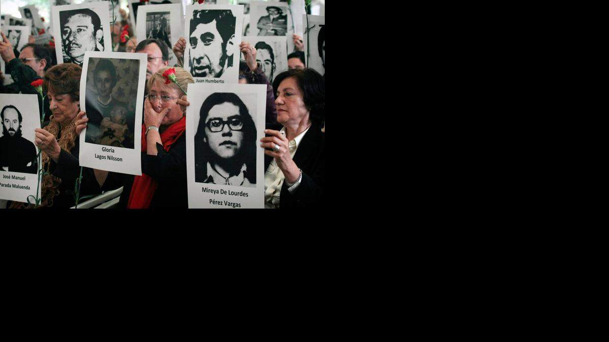 
La presidenta chilena Michelle Bachelet (cent.) se seca las lágrimas junto a su madre, Angela Jeria, (izq.); mientras sostienen fotos de las víctimas de la dictadura de Augusto Pinochet, en Santiado de Chile.
