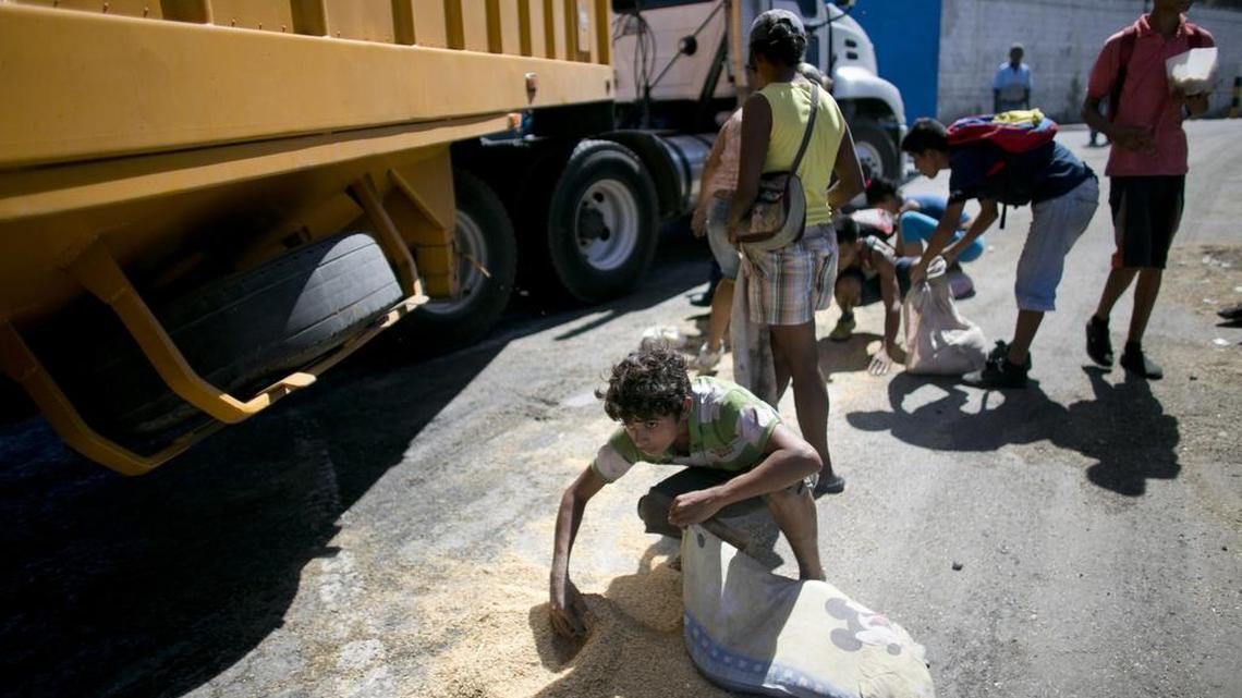 Un niño recoge arroz derramado sobre el pavimento desde un camión que espera en Puerto Cabello para distribuir su mercancía.