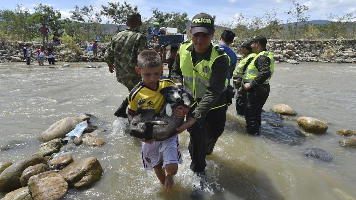 
Un niño colombiano cruza el jueves el río Táchira, en la frontera con Venezuela, con la asistencia de un efectivo de la policía de Colombia.
