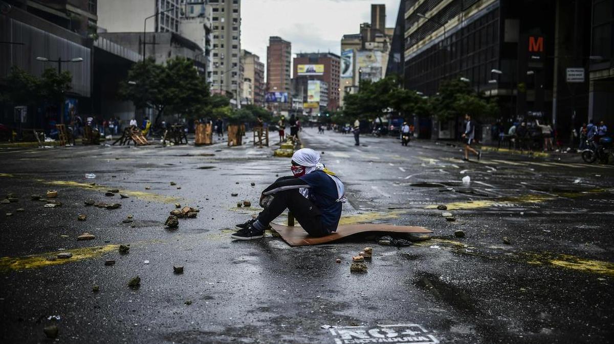 Un opositor enmascarado se sienta en medio de una avenida desierta y llena de escombros en Caracas el jueves. La huelga general convocada contra la Constituyente paralizó la mayor parte del país.