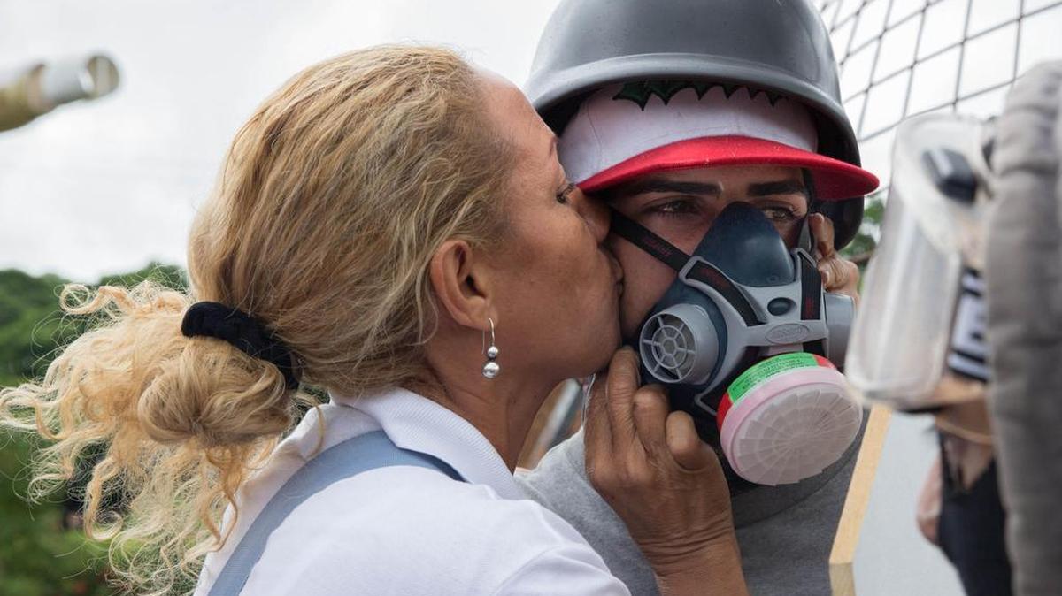 Una mujer besa en la mejilla a un manifestante que usa máscara antigases el sábado 24 de junio de 2017, en Caracas (Venezuela).