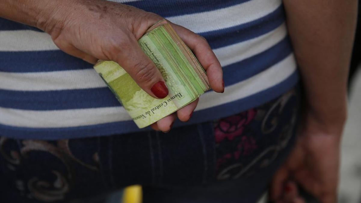 FILE - In this Feb. 7, 2018 file photo, a woman holds a wad of bills to pay her bus fare in Caracas, Venezuela. The IMF predicted on Monday, July 23, 2018 that inflation in Venezuela would reach one million percent this year, comparable to that experienced in Germany at the beginning of the 20th century and in Zimbabwe at the beginning of the last decade. (AP Photo/Ariana Cubillos, File)