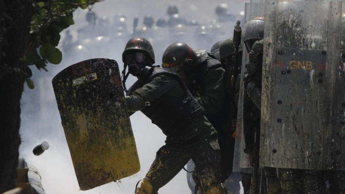 Miembros de la Guardia Nacional Bolivariana se protegen de un frasco lanzado contra ellos por manifestantes en Caracas, Venezuela, el miércoles 10 de mayo de 2017.