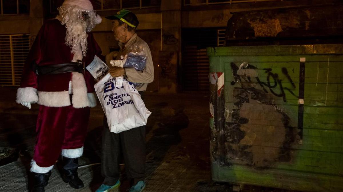 Un joven vestido de Santa Claus entrega regalos a un habitante de calle hoy, sábado 3 de diciembre de 2016, en el barrio La Vega de Caracas (Venezuela). La Fundación Santa en Las Calles recolectó ropa, comida, y juguetes para personas necesitadas y los entregó en barrios, asilos y calles caraqueñas.