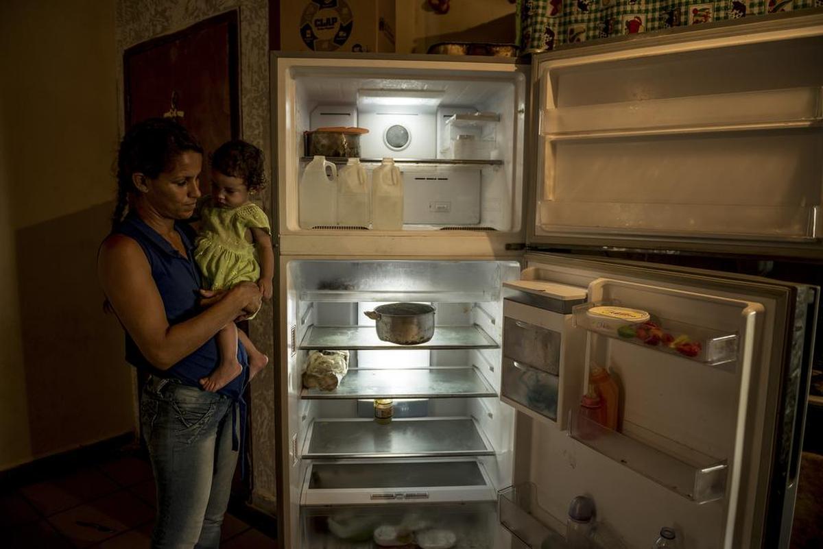 Wuendy Pérez, una madre soltera de cinco niños, sostiene a la menor, Wuendy Joselin, de 1 año, y muestra una nevera casi vacía en su vivienda en La Guaira, Venezuela, el 16 de junio. El colapso económico del país ha causado que muchas familias no tengan suficiente comida, lo que ha aumentado la desnutrición en los niños.
