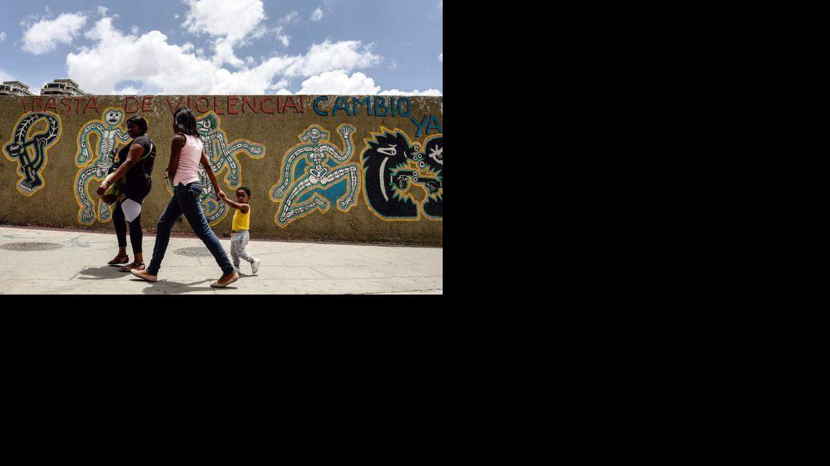 Foto de archivo. Mujeres caminan por una pared pintada con un mensaje que dice: "Basta de violencia - Cambiar ahora " en Caracas el 10 de septiembre de 2014.