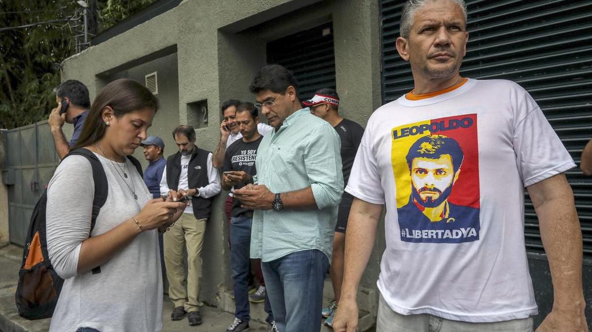 Familiares, militantes del partido Voluntad Popular, junto a miembros del Servicio Bolivariano de Inteligencia Nacional (Sebin), permanecen en la entrada de la casa en Caracas del opositor venezolano Leopoldo López que ha abandonado la cárcel y ha pasado a estar en una situación de "arresto domiciliario".