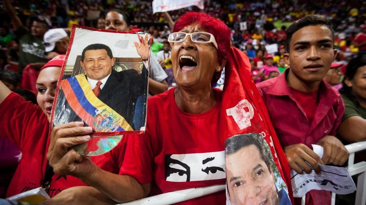 Una mujer sostiene una fotografía del fallecido presidente venezolano Hugo Chavez (izq.) y la foto del candidato a diputado, el oficialista William Ojeda, durante un evento de campaña, en Caracas. (Venezuela). EFE/MIGUEL GUTIÉRREZ