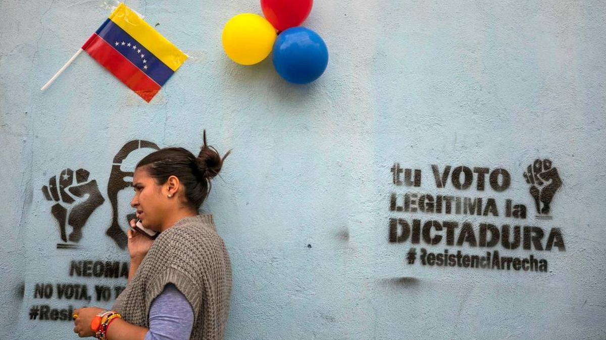 na mujer aguarda en las inmediaciones de un centro electoral con grafitis en las paredes que llaman a la abstención el domingo 15 de octubre de 2017, en Caracas (Venezuela).