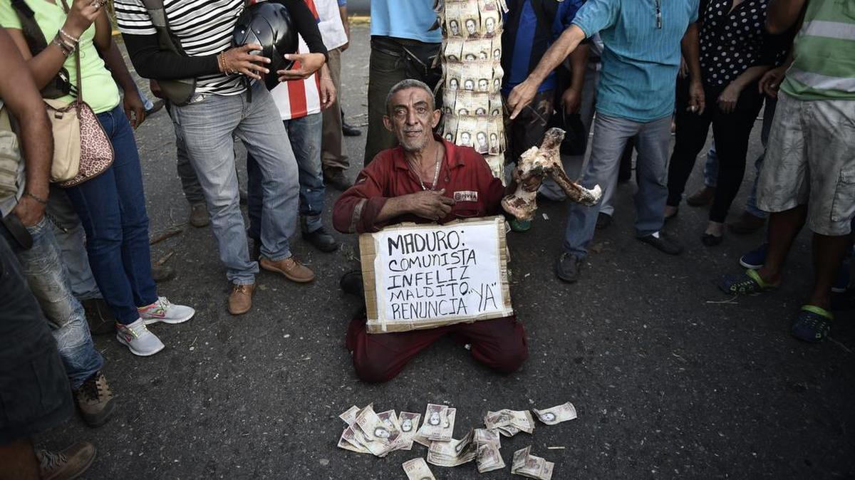 Un hombre sostiene un hueso y varios billetes de 100 bolívares para protestar contra la crisis monetario y ecómica de Venezuela en El Pinal, estado Táchira.