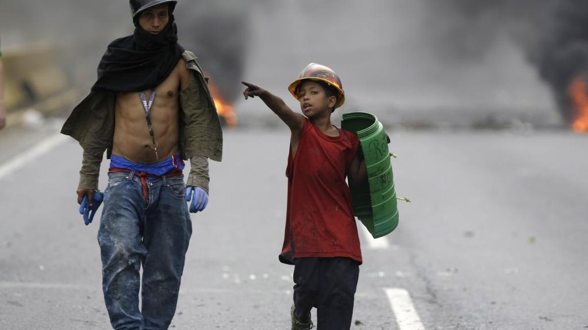 Un niño y un hombre caminan en una carretera bloqueada durante una protesta nacional contra el presidente Nicolas Maduro, en Caracas, Venezuela, el lunes 15 de mayo de 2017.