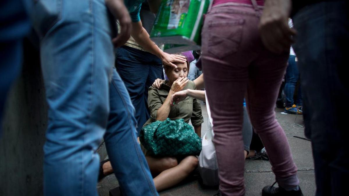 Una mujer se desmaya tras varias horas en una cola para comprar algunos alimentos en un mercado en Caracas.