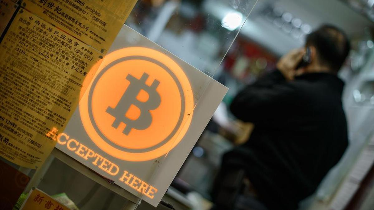 Esta image de archivo tomada el 28 de febrero de 2014 muestra a un hombre hablando por teléfono móvil en una tienda mostrando un signo de bitcoin durante la ceremonia de apertura de la primera tienda minorista bitcoin en Hong Kong. Miles de venezolanos han comenzado a extraer bitcoins, la criptomoneda, para evitar la hiperinflación.