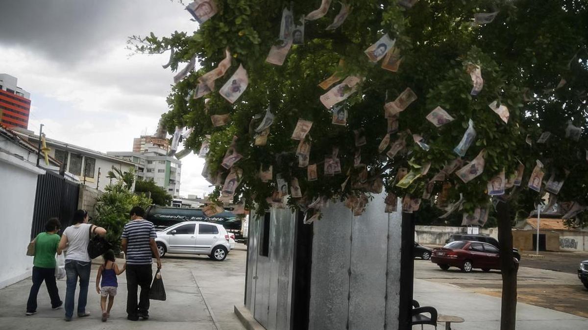 Personas caminan frente a un árbol con billetes venezolanos colocados en sus ramas como protesta a la situación económica, el 27 de diciembre del 2017, en Maracaibo.