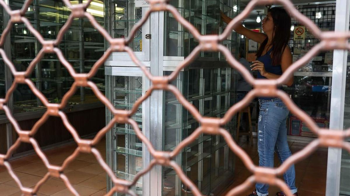 Una mujer organiza productos en el mostrador de un local cerrado al público el 21 de agosto de 2018, durante el primer día laboral tras la reconversión monetaria en el centro de Caracas (Venezuela).