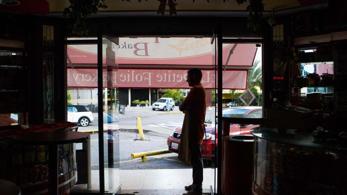 Trabajadores y clientes de comercios y restaurantes esperan a que se resuelva una falla eléctrica, el lunes 18 de diciembre de 2017, en Caracas, Venezuela.