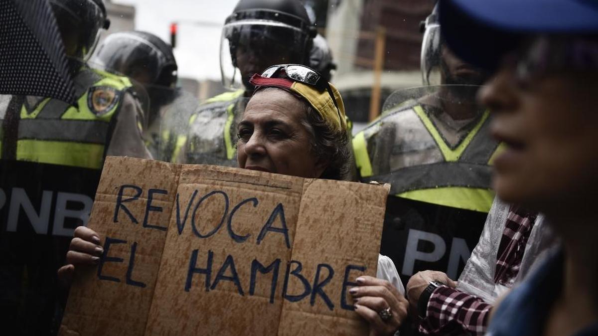 Una manifestante sostiene un afiche en el que pide revocar el hambre, mientras es rodeada por agentes de la Policía Nacional, en Caracas, en julio.