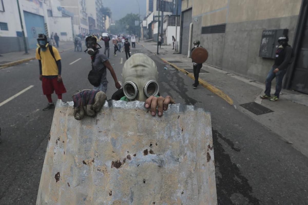 Un joven con máscara de gas se refugia detrás de un trozo de techo corrugado durante las protestas contra el gobierno en Caracas, Venezuela, el miércoles 19 de abril de 2017. Decenas de miles de opositores al presidente Nicolás Maduro inundaron las calles de Caracas.