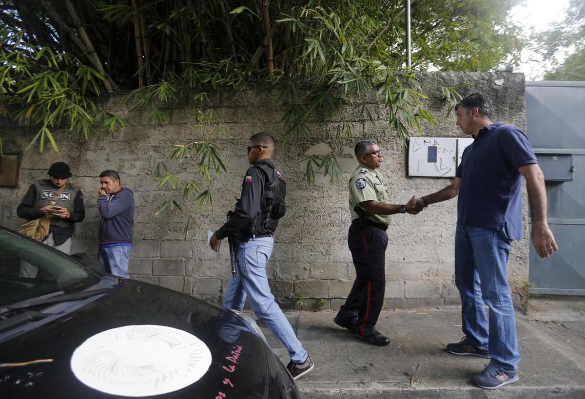 Oficiales de la policía secreta venezolana, SEBIN, a la izquierda, se colocan en guardia frente al líder opositor Leopoldo López mientras Alfredo Jimeno, a la derecha, saluda a un oficial de policía en Caracas, Venezuela, el sábado 8 de julio de 2017.