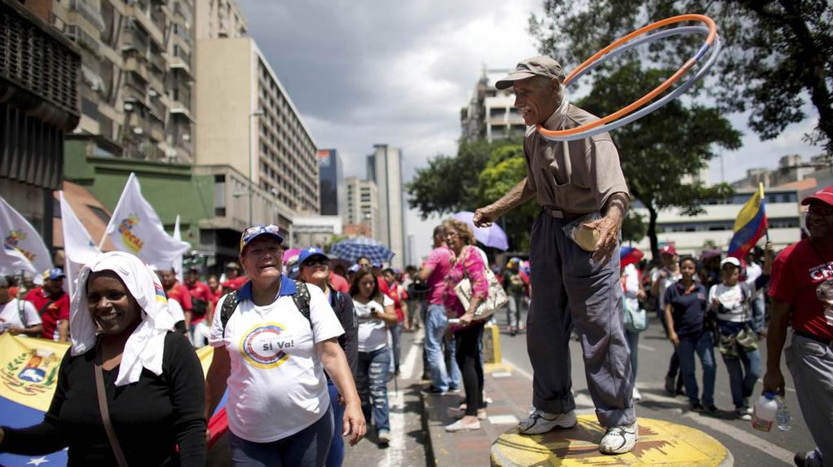 En esta foto del 19 de septiembre de 2017, los seguidores del gobierno marchan frente a un hombre que trabaja en la calle durante una manifestación anti-imperialista, en Caracas, Venezuela.