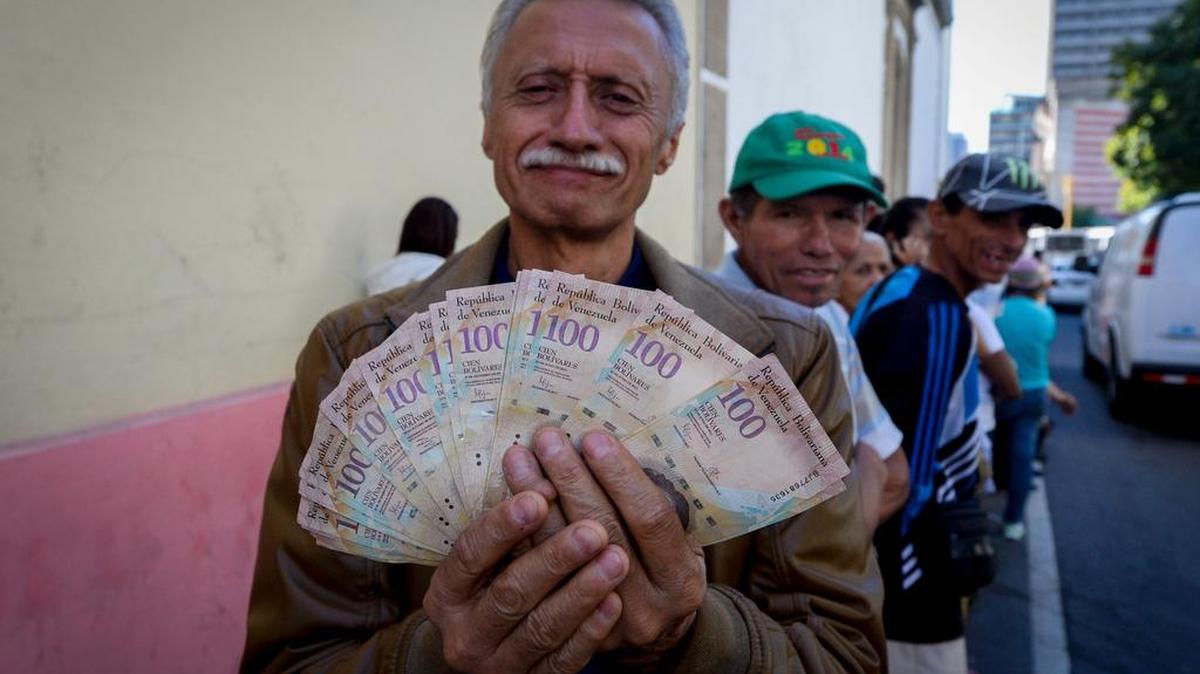 Un hombre muestra varios billetes de 100 bolívares mientras hace una fila fuera del Banco Central de Venezuela el 16 de diciembre de 2016.