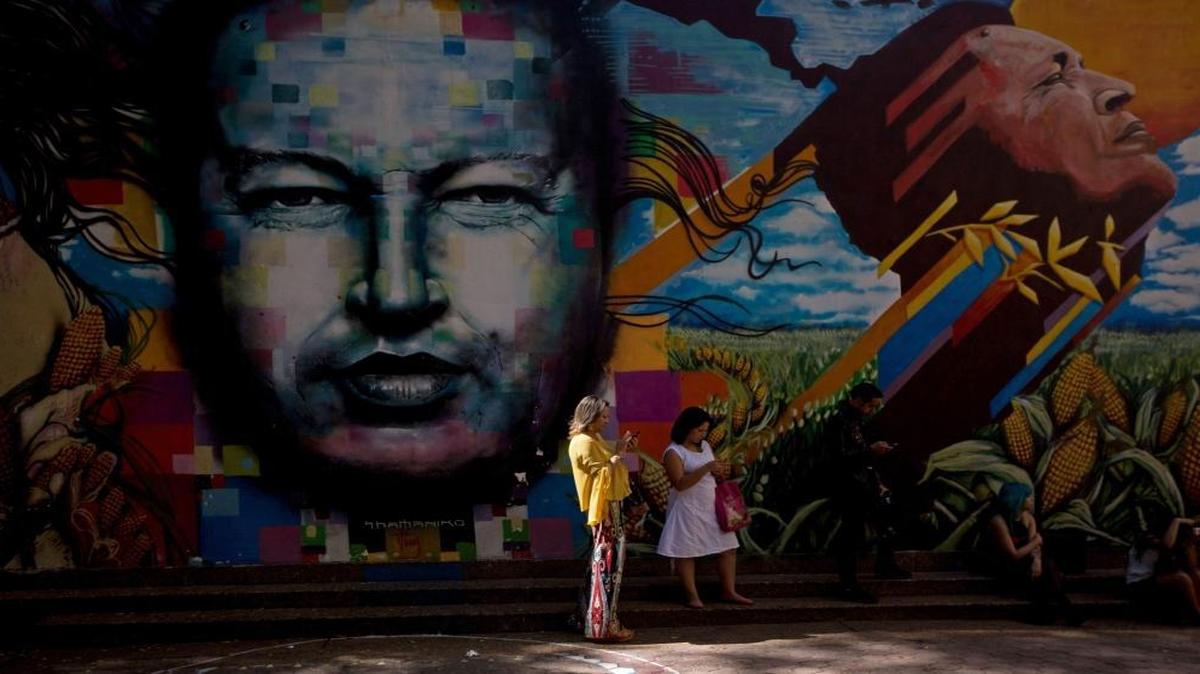 Dos mujeres se cubren del sol junto a un enorme mural de Hugo Chávez en el barrio 23 de Enero de Caracas en julio del 2014.