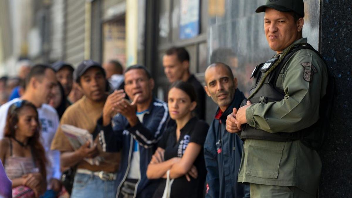 Un soldado vigila la entrada de un banca ante la mirada impaciente de cientos de personas que esperan en fila, el jueves en Caracas.