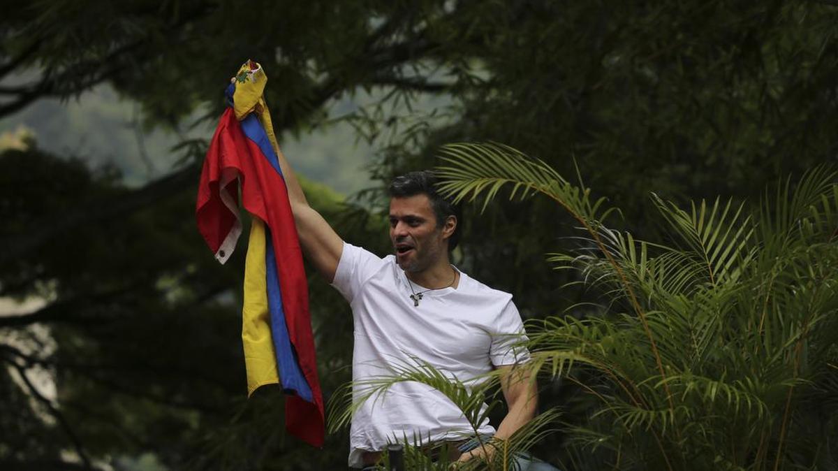El líder de la oposición Leopoldo López tiene una bandera nacional venezolana mientras saluda a sus partidarios fuera de su casa en Caracas, Venezuela, el sábado 8 de julio de 2017.