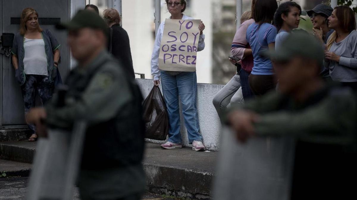 Una mujer sostiene un cartel en el que se lee "Yo soy "scar Pérez" frente a miembros de la Guardia Nacional Bolivariana y la Policía Nacional Bolivariana que custodian las inmediaciones de la morgue en donde está cuerpo del ex agente Pérez el miércoles 17 de enero de 2018, en Caracas (Venezuela).