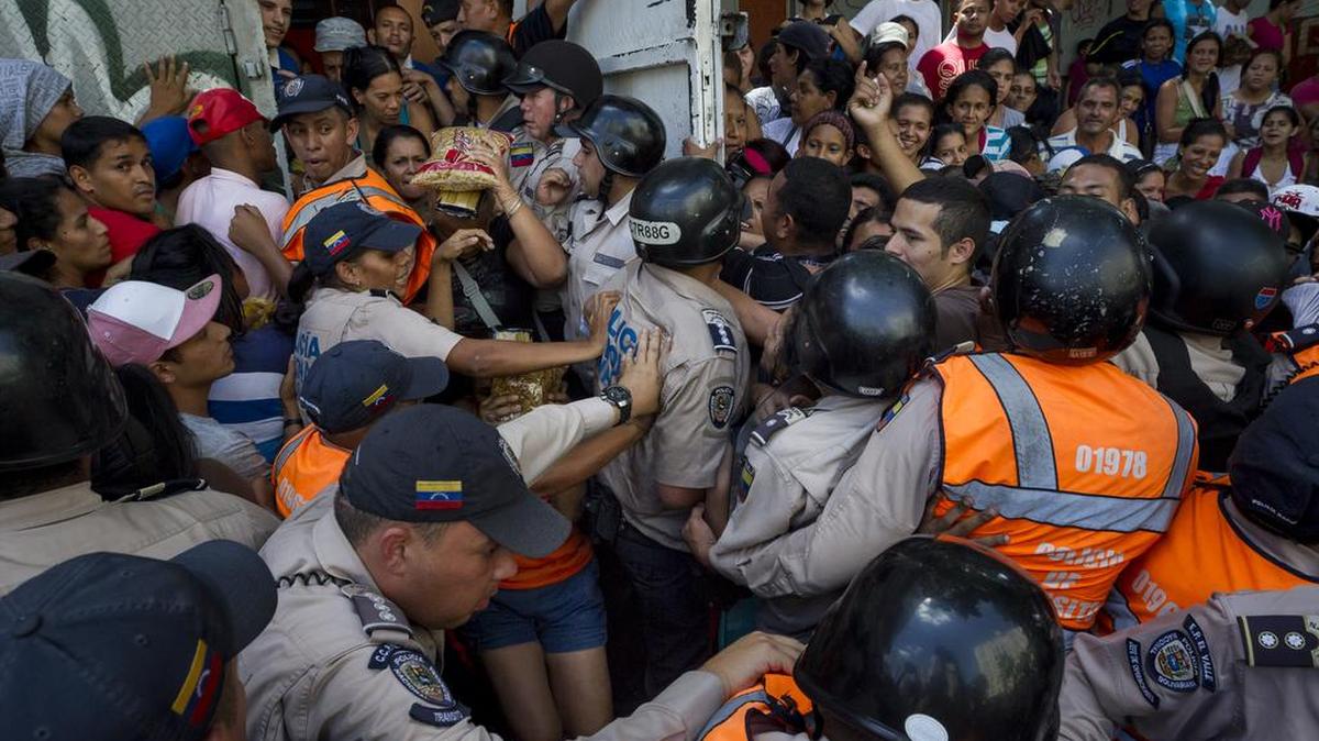 Miembros de la Policía Nacional Bolivariana contienen a un grupo de personas que trata de ingresar a un supermercado donde se venden dos kilos de pasta por persona en Caracas.