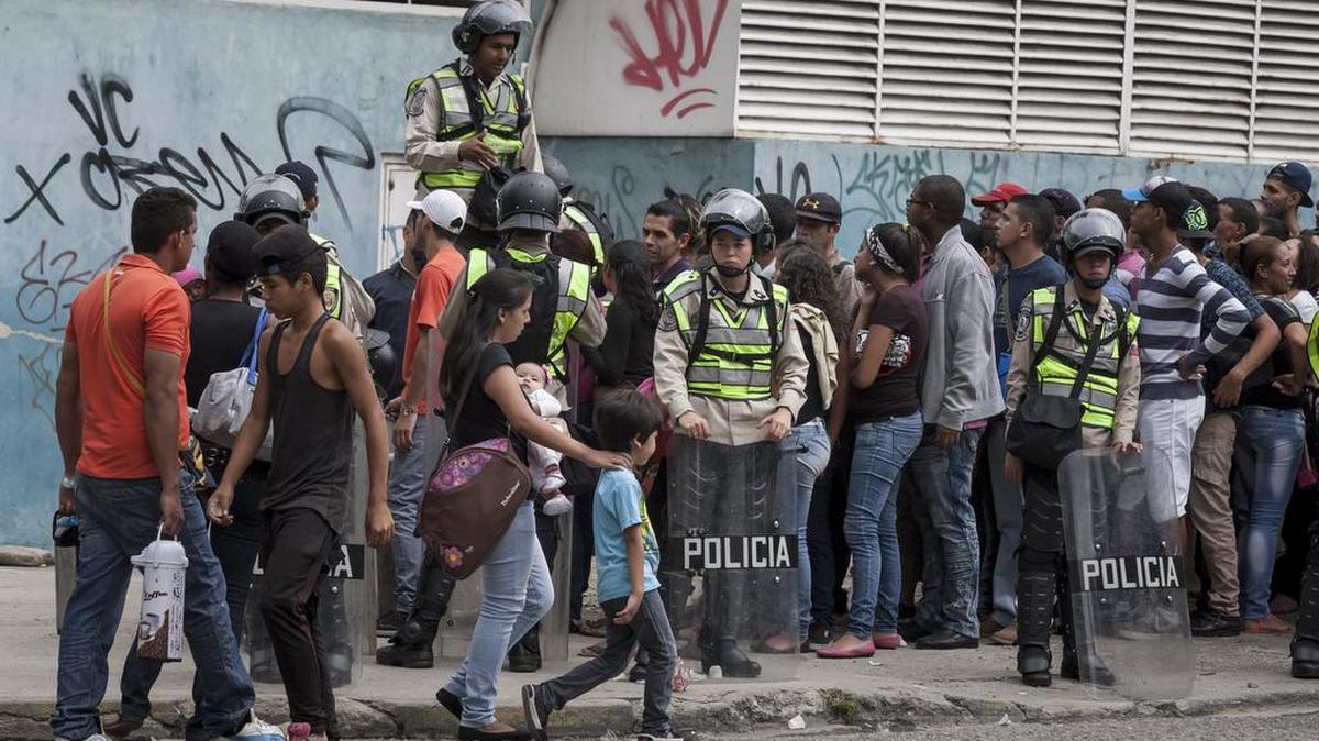 Miembros de la Policía Nacional Bolivariana (PNB) custodian el miércoles el orden público de una fila de personas que aguardan para poder entrar a un supermercado y comprar productos.