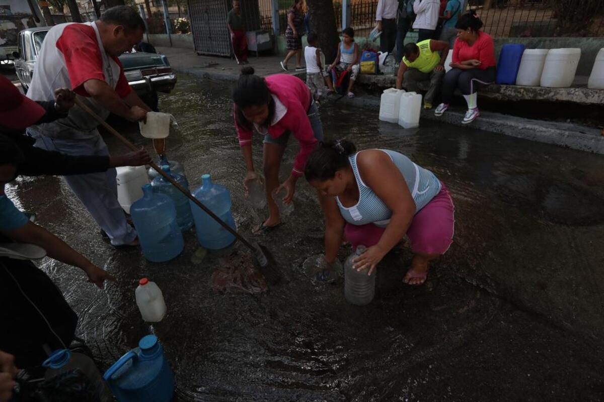 Un grupo de personas intenta recolectar agua en el sistema de alcantarillado el martes ante la escasez del líquido por el apagón eléctrico en Caracas (Venezuela).