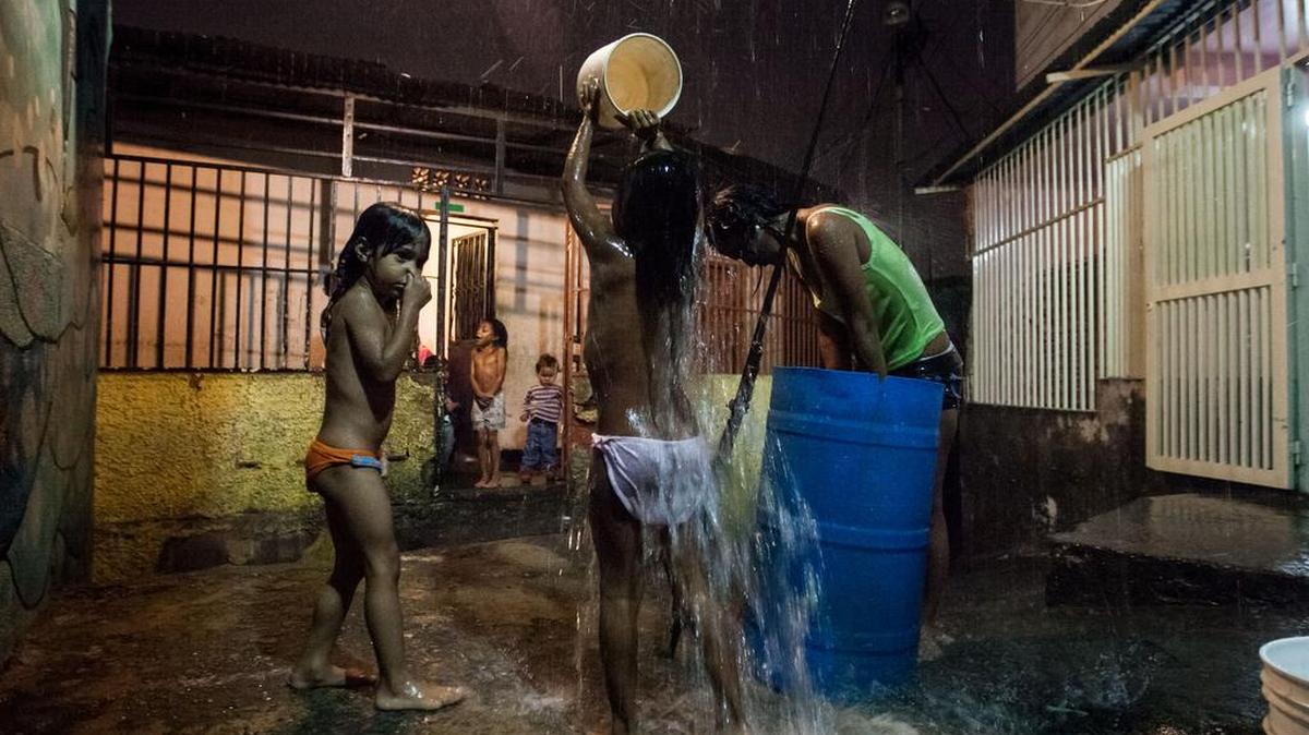 Fotografía del 22 de abril del 2016, donde se observa a un grupo de personas bañándose con agua de lluvia en un callejón en La Bombilla, en la populosa favela de Petare en la ciudad de Caracas (Venezuela). Era de noche cuando Ana debía tomar el baño, sabía que era el momento no por la hora, sino por el sonido que hace el drenaje de los techos de las casas cuando corre la lluvia. Las consecuencias del fenómeno climático El Niño, que ha ocasionado los dos años de sequía más extrema vividas en el país, han puesto contra la pared al país petrolero no solo por la distribución de agua sino también porque depende de la generación hidroeléctrica en más de un 60 por ciento.