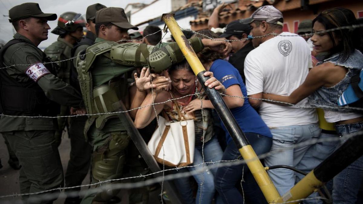 Un grupo de personas trata de cruzar hacia territorio colombiano mientras miembros de la Guardia Nacional Bolivariana resguardan un punto de control en la población de Ureña, en Venezuela.