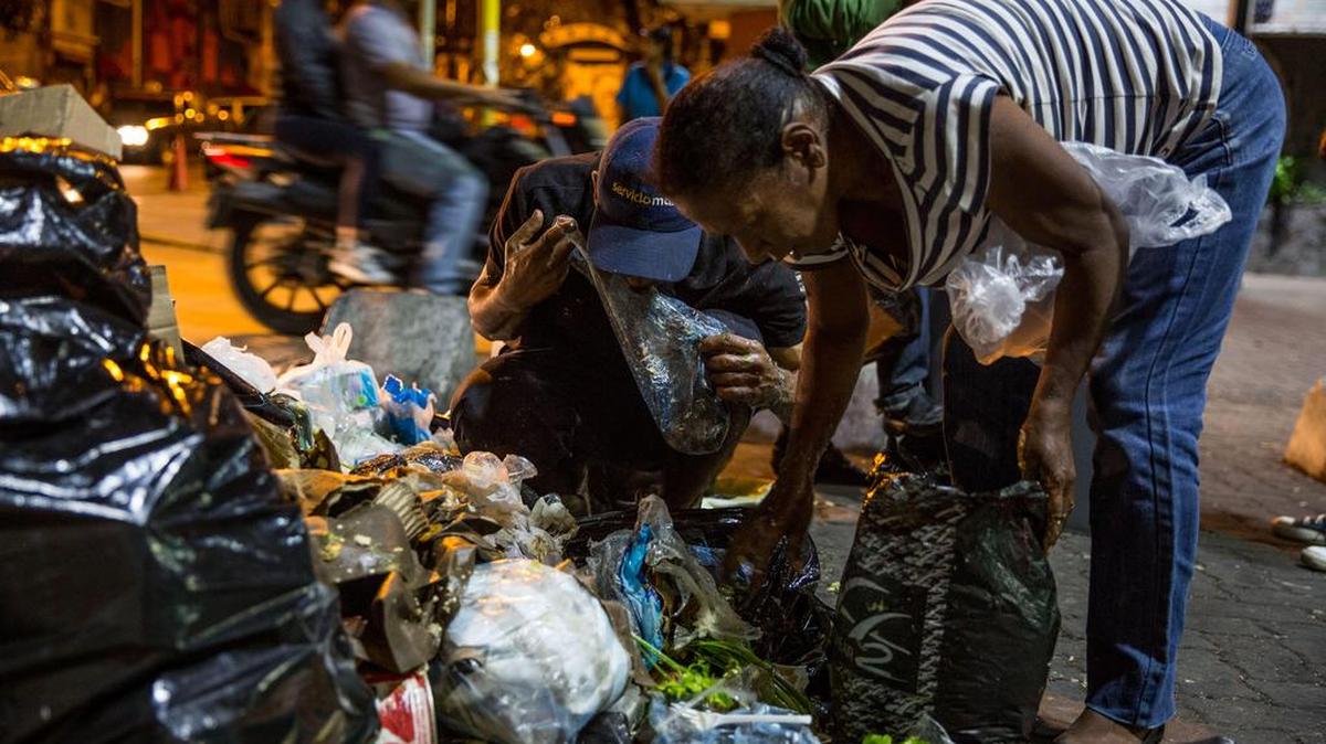Varias personas buscan comida entre bolsas de basura este jueves, 31 de diciembre de 2016, en Caracas (Venezuela). La profunda crisis que aqueja a Venezuela trajo como consecuencia escasez y hambre, lo que a su vez ha llevado a familias enteras a buscar restos de alimentos en los basureros y, muchas veces, a pelear con otras personas sin recursos, por un desecho comestible o algún material reciclable que se pueda vender.