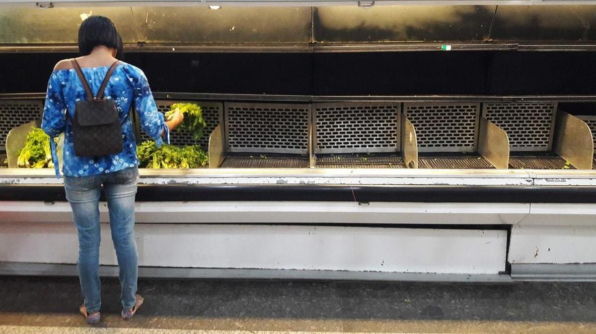 Una mujer escoge vegetales en un estante refrigerado prácticamente vacío en un supermercado en Caracas el 11 de enero del 2018.