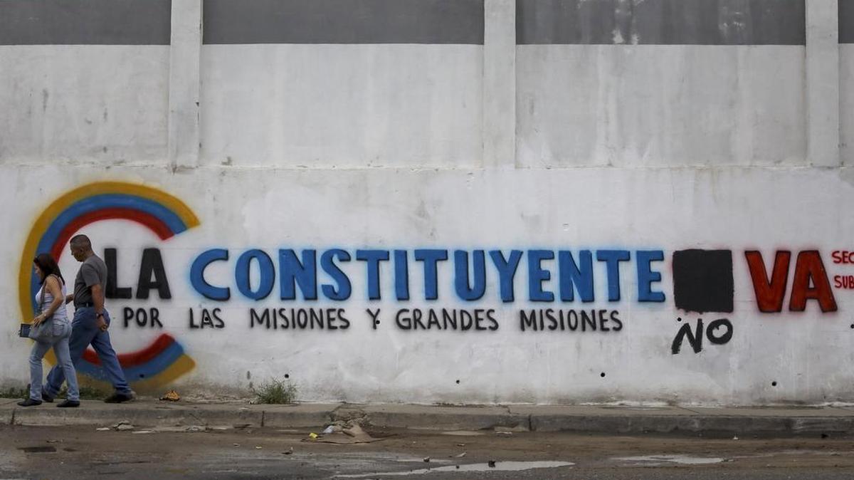 Un pareja camina frente a una pared con propaganda de la Asamblea Nacional Constituyente, el sábado 15 de julio de 2017, en Caracas, Venezuela.