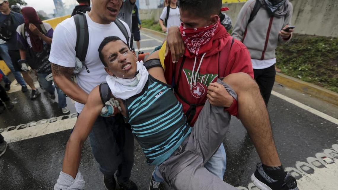 Dos manifestantes ayudan a un compañero afectado por los gases lacrimógenos durante una protesta contra el gobierno de Venezuela, el jueves en Caracas.