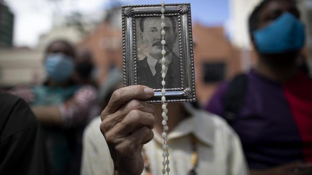 Un devoto sostiene una imagen enmarcada del difunto Dr. José Gregorio Hernández frente a la iglesia La Candelaria en Caracas, donde están enterrados sus restos, el 26 de octubre del 2020.