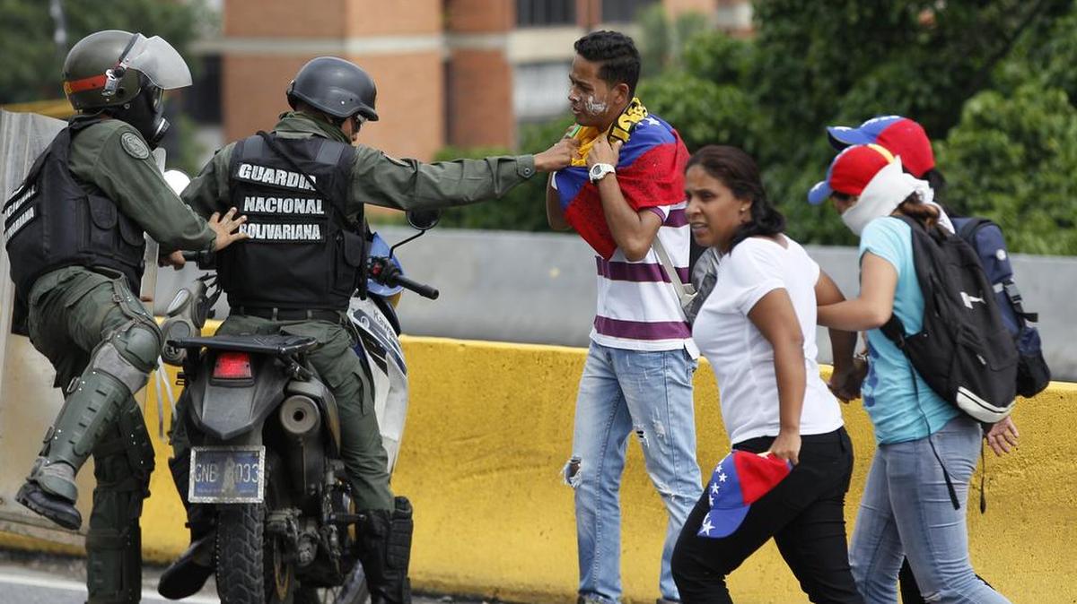Un miembro de la Guardia Nacional Bolivariana trata de quitar la bandera alrededor del cuello de un manifestante antes de dejarlo ir, después de que las fuerzas de seguridad bloquearan una marcha de la oposición en Caracas, Venezuela, el miércoles 24 de mayo de 2017.