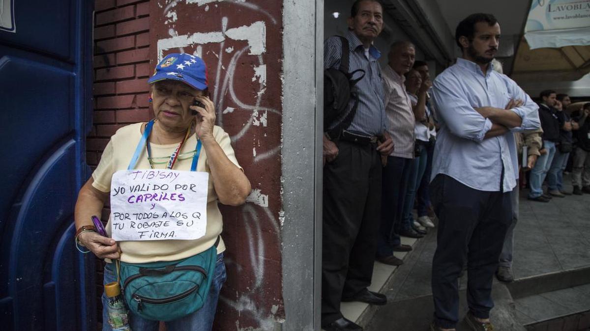 Una mujer muestra un carte el respaldo a la oposición venezolana el lunes 20 de junio, mientras una fila de personas espera para validar sus firmas para un referendo revocatorio.