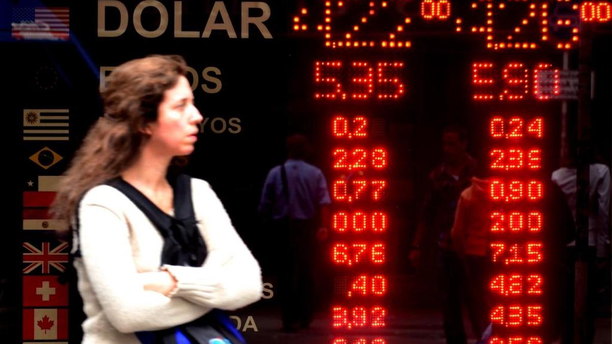 Una mujer pasa frente a una cartelera electrónica que muestra las tasas de cambio del mercado cambiario, en Buenos Aires, Argentina. Foto archivo.