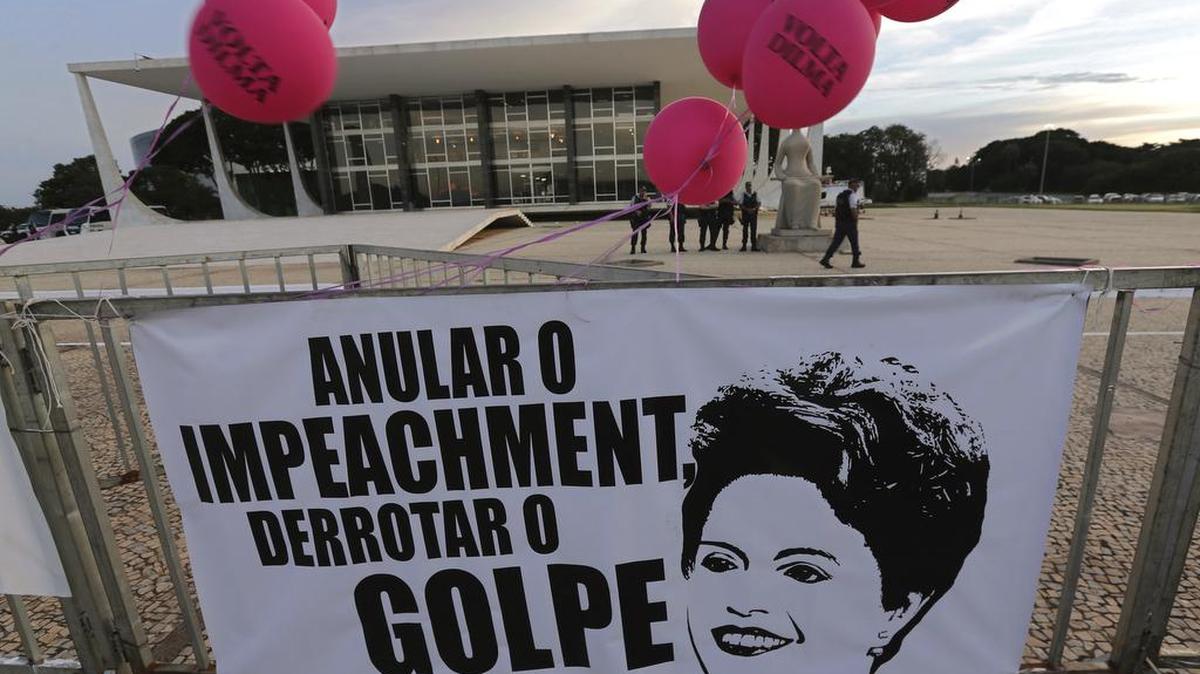 Un cartel muestra una imagen de la ex presidenta de Brasil Dilma Rousseff y el mensaje en portugués: "Cancelar el juicio político, derrotar el golpe" fuera de la Corte Suprema durante una protesta que marca el Día Internacional de la Mujer en Brasilia, Brasil, el miércoles 8 de marzo de 2017.